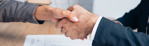 panoramic crop of businessman and businesswoman shaking hands in office