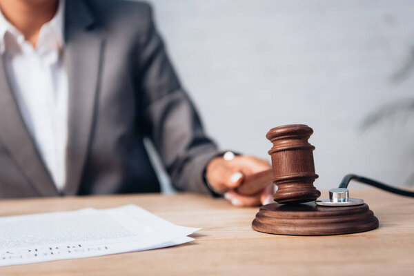 cropped view of judge holding gavel near stethoscope and documents 