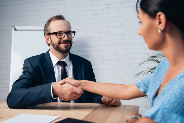 selective focus of bearded lawyer in glasses shaking hands with client in office 