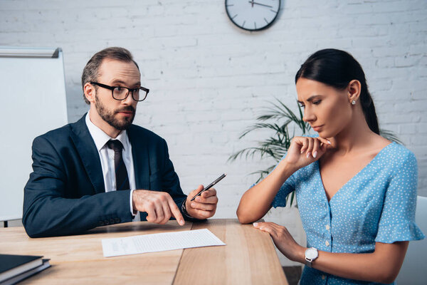 bearded lawyer in glasses pointing with finger at insurance contract while holding pen near woman in office 