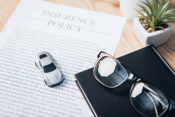 toy car on insurance policy agreement near notebook, plant and glasses 