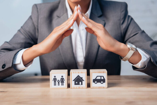 cropped view of lawyer holding hands above wooden cubes with family, car and house 