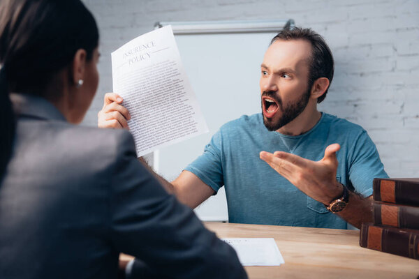 selective focus of angry and bearded man screaming while holding insurance policy agreement near lawyer 