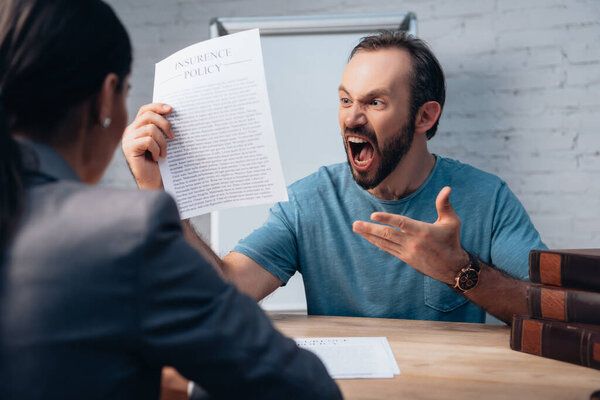selective focus of angry man screaming while holding insurance policy agreement near lawyer 