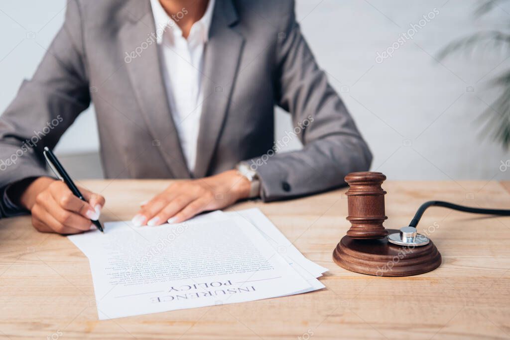 cropped view of judge signing insurance policy contract near gavel and stethoscope 