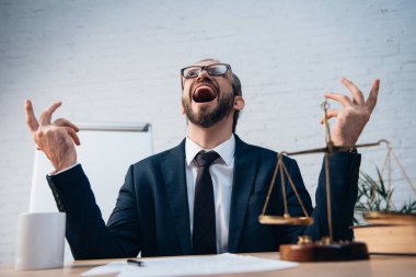selective focus of excited and bearded lawyer with open mouth looking up while gesturing in office clipart
