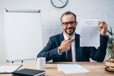 selective focus of lawyer in glasses holding pen and contract with insurance policy lettering in office clipart