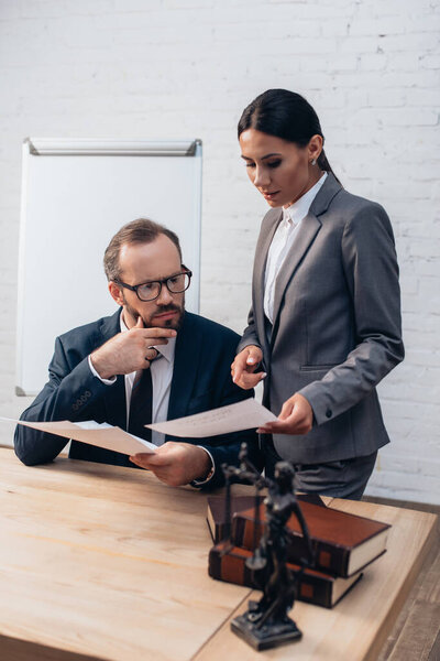 избирательный фокус бородатого адвоката в очках, смотрящего на документы, в то время как коллега показывает пальцем в офисе