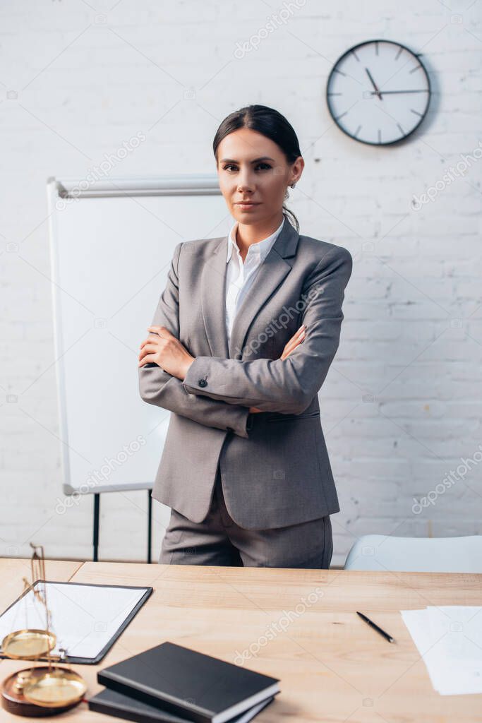 brunette lawyer in formal wear standing with crossed arms in office