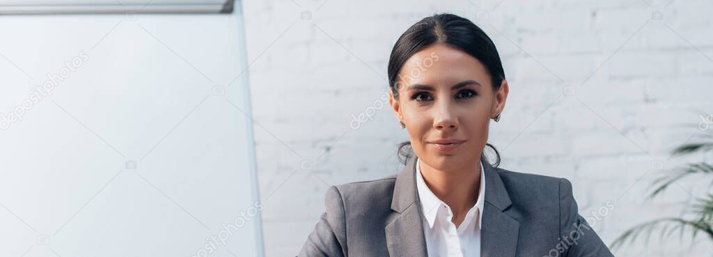 panoramic crop of brunette lawyer in formal wear looking at camera in office