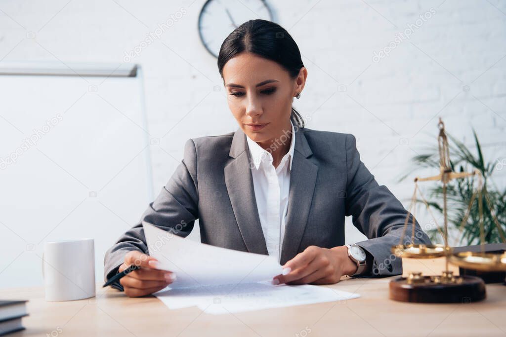 selective focus of brunette lawyer in formal wear looking at insurance documents in office