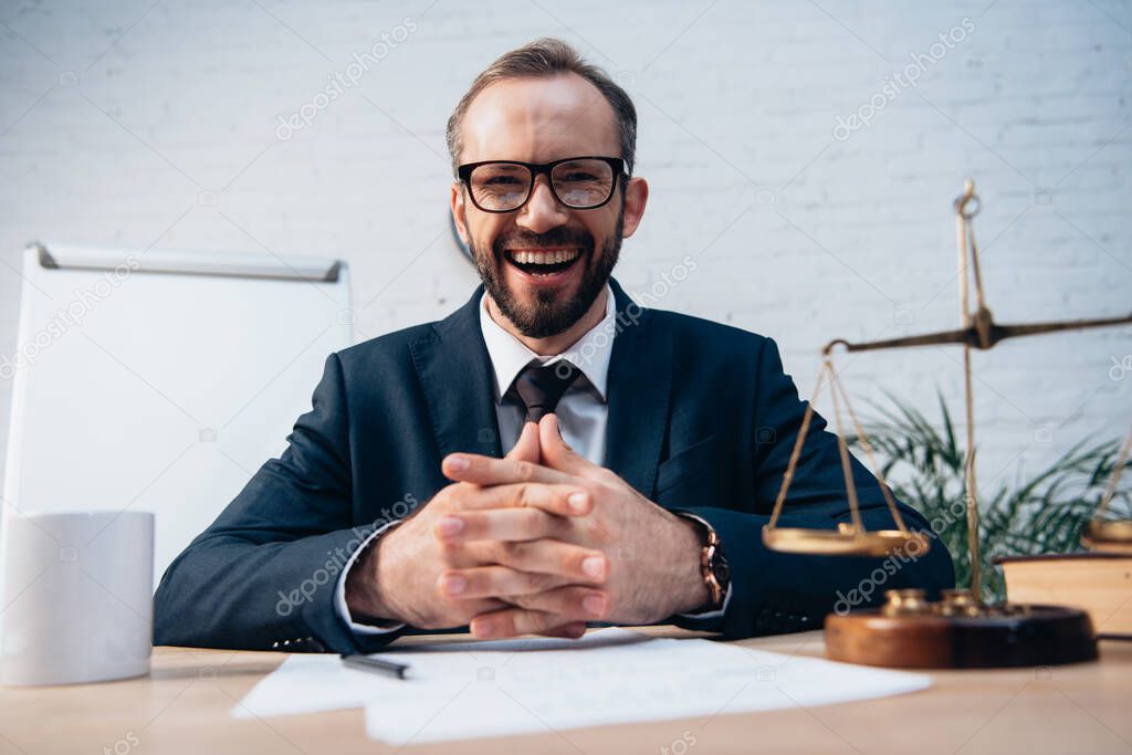 selective focus of excited and bearded lawyer sitting with clenched hands at desk