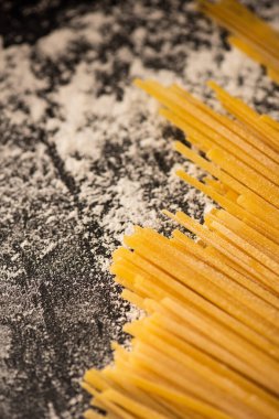close up view of raw spaghetti and flour on black background clipart