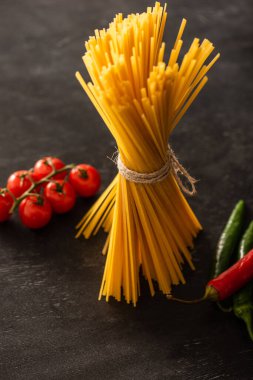 Pişmemiş İtalyan spagettisi, domatesli ve siyah arka planda kırmızı biberli.