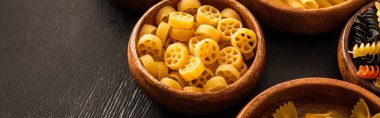 raw Italian Rotelle pasta in wooden bowl on black background, panoramic shot clipart