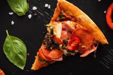 Lezzetli İtalyan pizza diliminin üst görüntüsü fesleğen yapraklarının yanında salam ve siyah arka planda tuz.