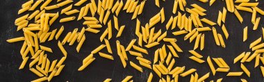 top view of raw penne pasta scattered on black background, panoramic shot clipart