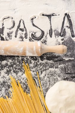 Yuvarlak iğne, hamur ve makarnanın yanındaki çiğ spagetti, siyah arka planda un üzerine.