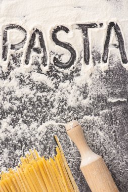 Yuvarlanan iğnenin yanında çiğ spagetti ve siyah arkaplanda un üzerine makarna.