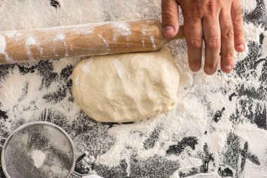 cropped view of man rolling out dough on flour on black background clipart