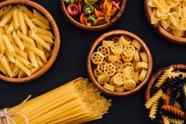 top view of assorted colorful Italian pasta in wooden bowls on black background clipart