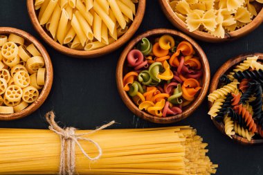 top view of assorted colorful Italian pasta in wooden bowls on black background clipart