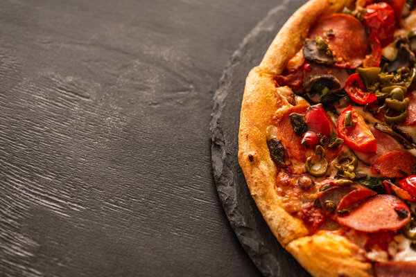 top view of delicious Italian pizza with vegetables and salami on black wooden background