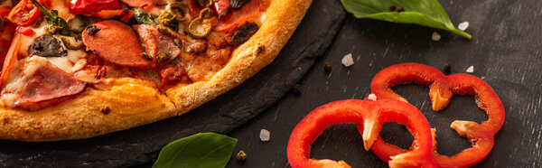 close up view of delicious Italian pizza with salami near vegetables on black background, panoramic shot
