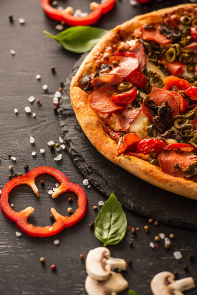 selective focus of delicious Italian pizza with salami near vegetables on black background