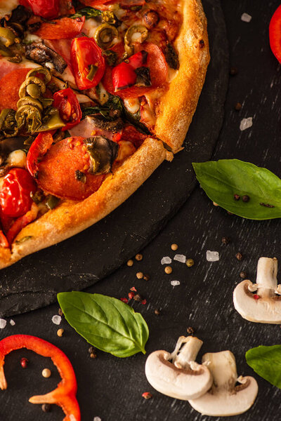 close up view of delicious Italian pizza with vegetables and salami on black background