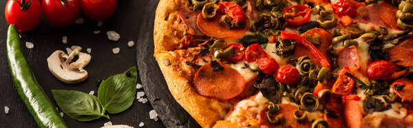 delicious Italian pizza with salami near vegetables on black background, panoramic shot