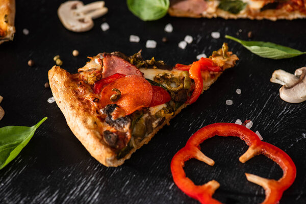 delicious Italian pizza slice with salami near vegetables on black background