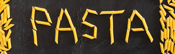 top view of pasta word made of raw penne on black background, panoramic shot