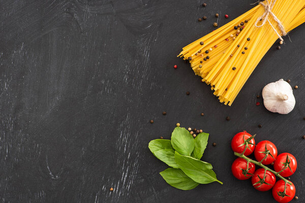 top view of raw Italian spaghetti with vegetables and spices on black background