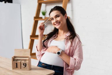 selective focus of pregnant woman touching belly near wooden cubes with date clipart