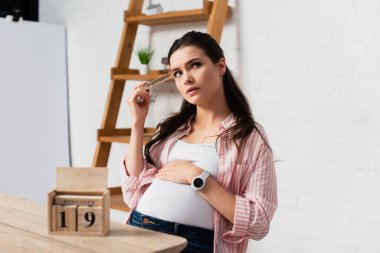 selective focus of thoughtful and pregnant woman touching belly near wooden cubes with date clipart