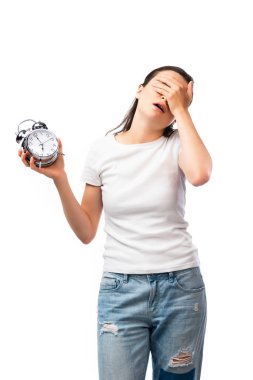 tired woman in white t-shirt and jeans holding retro alarm clock while covering face isolated on white clipart