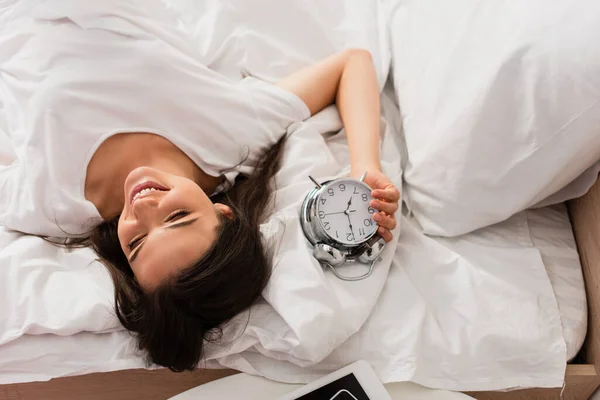 レトロな目覚まし時計とベッドの上に横たわるブルネットの女性のトップビュー — ストック写真