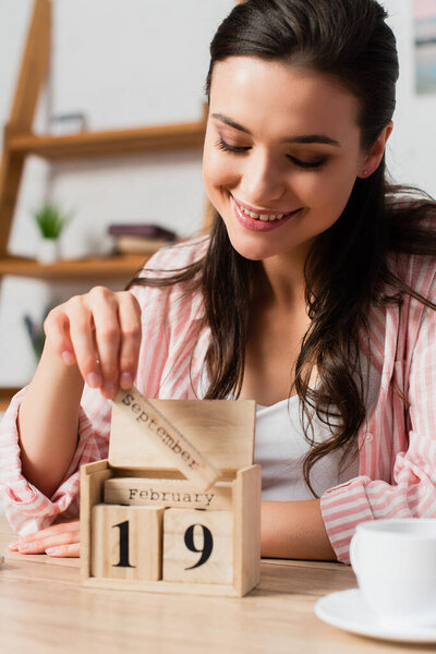selective focus of woman touching wooden cubes with date near cup 