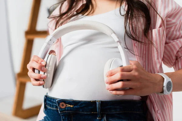 Vista Recortada Mujer Embarazada Sosteniendo Auriculares Inalámbricos Cerca Del Vientre — Foto de Stock