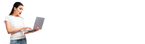 панорамный урожай потрясенной брюнетки в белой футболке с ноутбуком, изолированным на белом 
