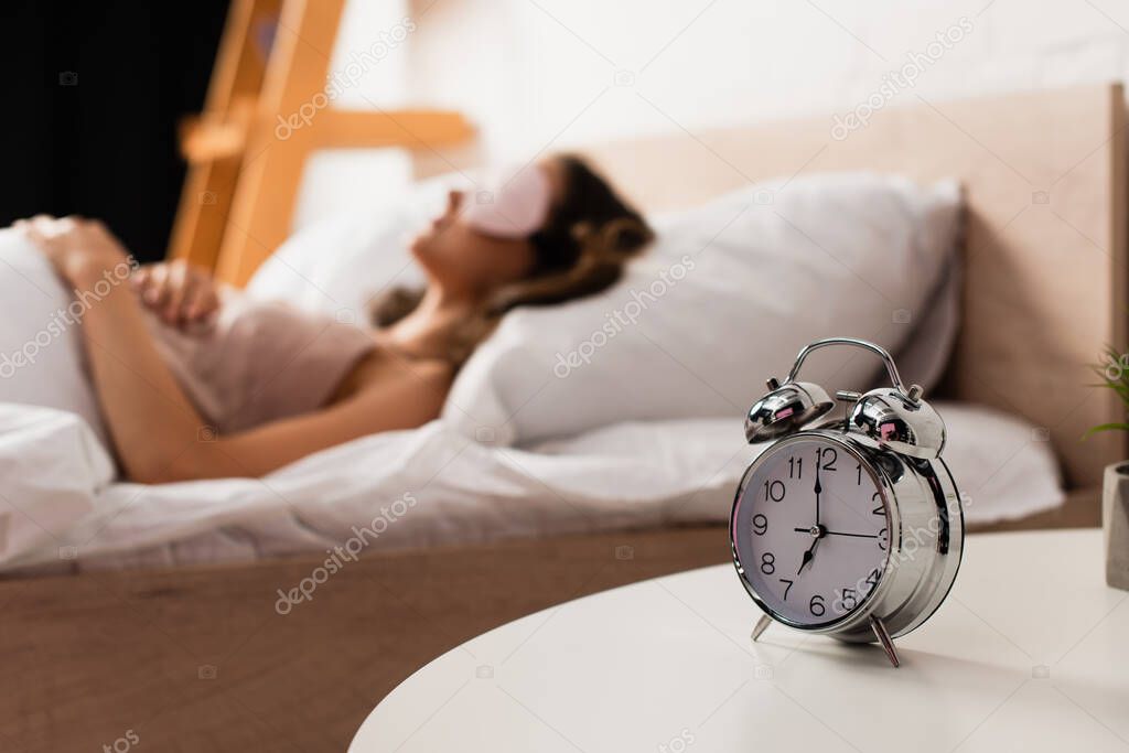 selective focus of alarm clock on bedside table near woman sleeping on bed