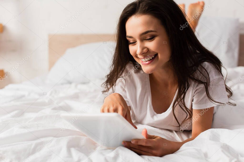 selective focus of young woman lying on bed and using digital tablet 