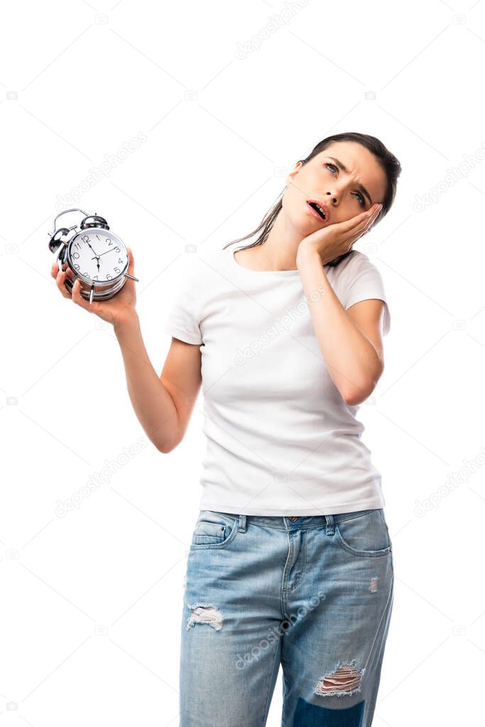 tired brunette woman in white t-shirt and jeans holding retro alarm clock isolated on white