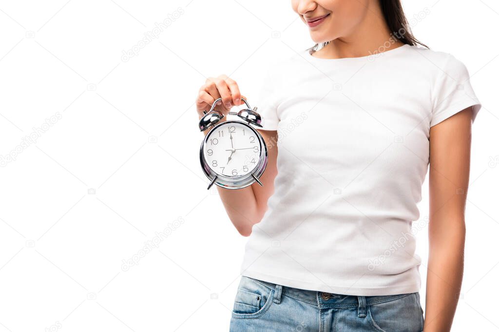 partial view of young woman in white t-shirt holding vintage alarm clock isolated on white