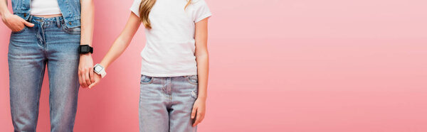 cropped view of mother and child in jeans and smartwatches holding hands on pink, website header