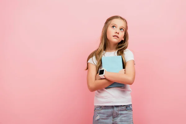 Στοχαστικό Παιδί Smartwatch Κοιτάζοντας Μακριά Ενώ Κρατώντας Βιβλίο Απομονωμένο Ροζ — Φωτογραφία Αρχείου