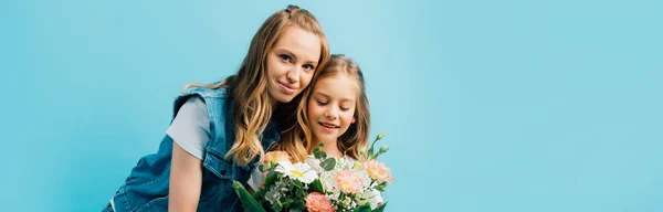 ブルーに孤立した花の花束を持つ娘の近くの若い女性のパノラマの概念 — ストック写真