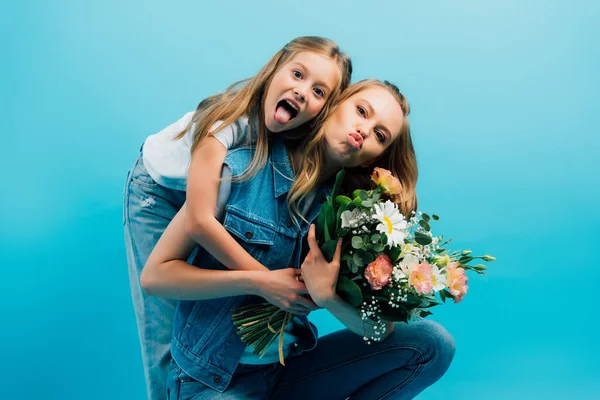 Chica Sobresaliendo Lengua Abrazando Madre Puchando Labios Mientras Sostiene Ramo — Foto de Stock