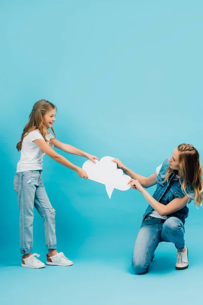 mother and daughter in jeans having fun while holding thought bubble on blue